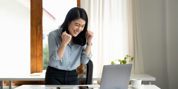 excited-young-woman-standing-at-table-with-laptop-2022-10-07-21-20-13-utc 1